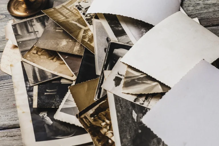 Fotografie di famiglia disposte su un tavolo, alcune girate sul retro, accanto a una scatola di ricordi.